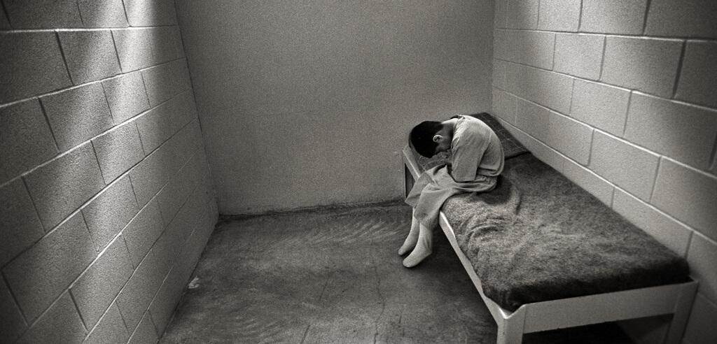 Small child alone in cell sitting on cot with head down